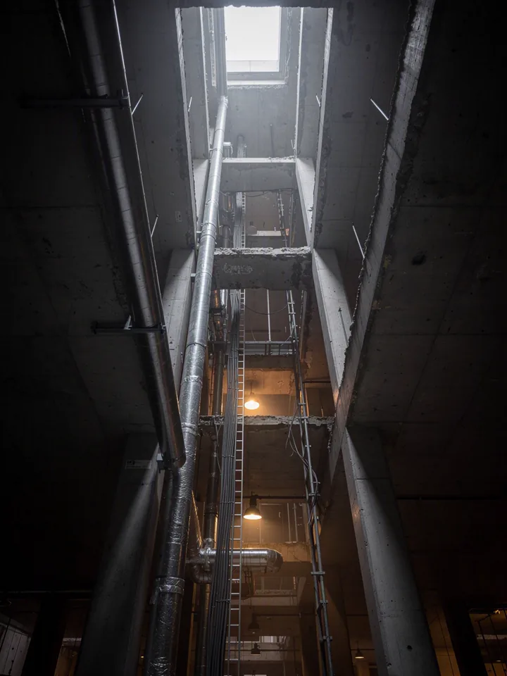 Looking up a vertical service shaft with bundled ducts, pipes and cable ladders